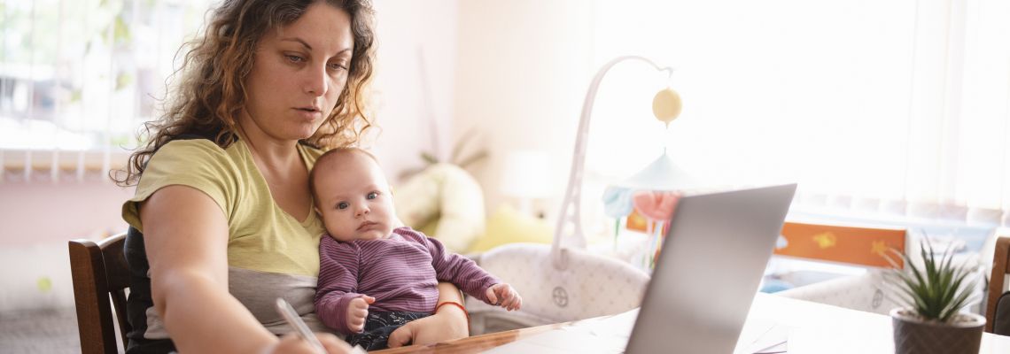 Mother is working on her laptop at her home while she is taking care for her newborn child