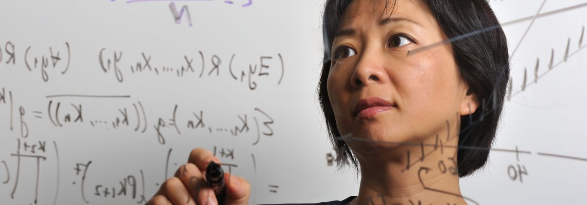 Portrait of Asian woman, in her 30s or 40s, working on some mathematical formulas on a translucent board.