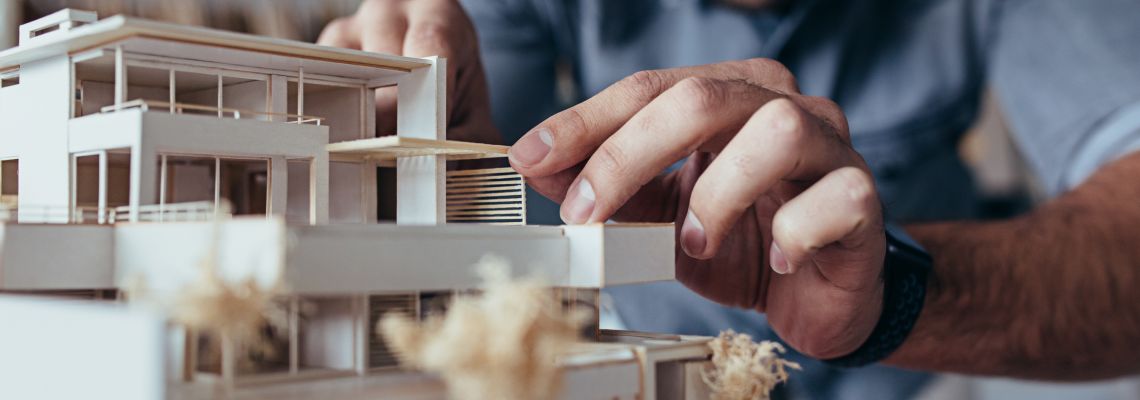Close up of male architect hands making model house. Man architect working in the office.