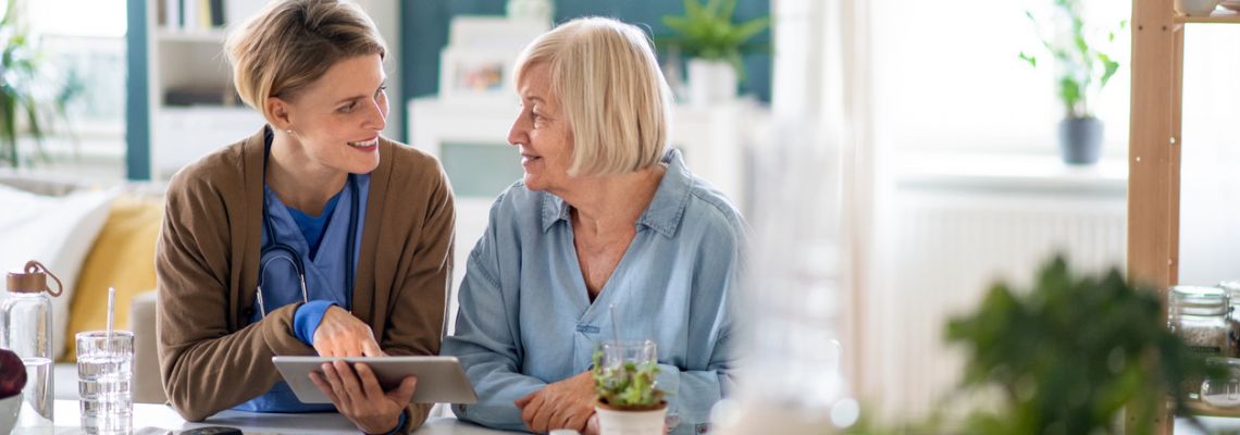 Caregiver or healthcare worker with senior woman patient, using tablet and explaining. Home health aide works with an elderly woman.