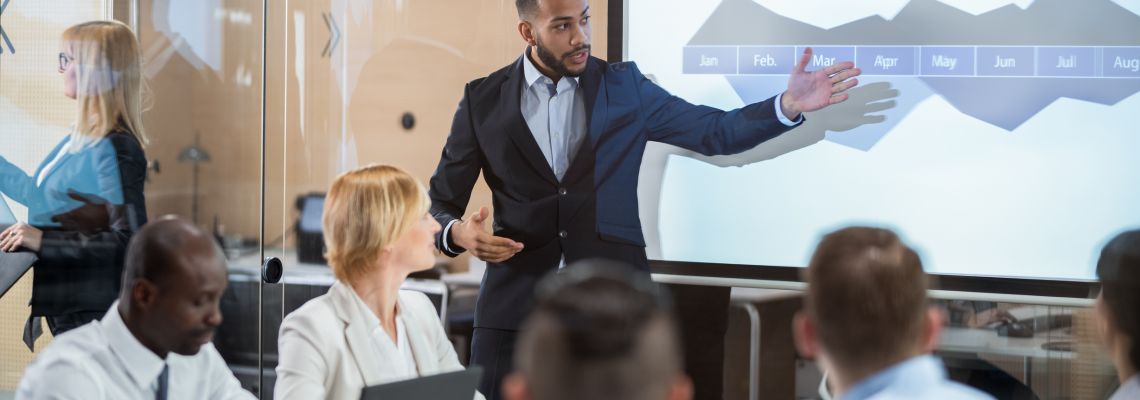 Financial Analyst Presenting A Graph To The Board Of Directors Man presents on the topic of MBA vs Master's in Management.