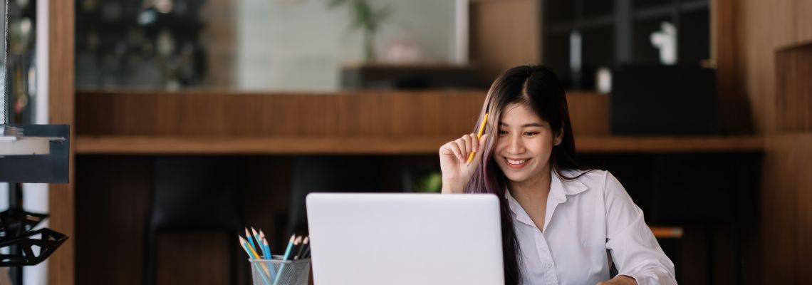 Young asian woman studying online via laptop computer for e-learning - Online Education Concept Student reads online guide to college accreditation before selecting an online program to attend.