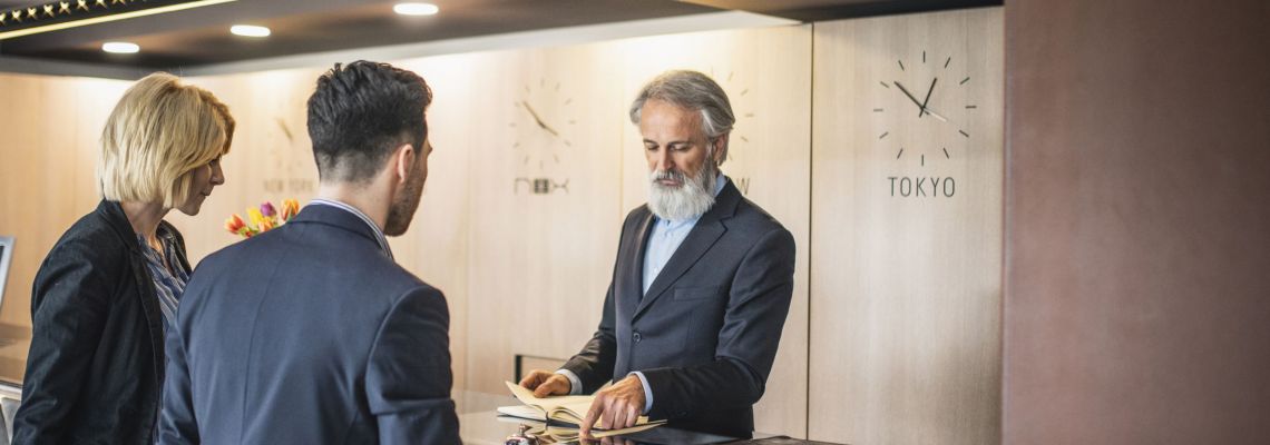 Hospitality Management Careers, Mature Hotel Receptionist Assisting Young Business Travelers Hospitality Management Careers