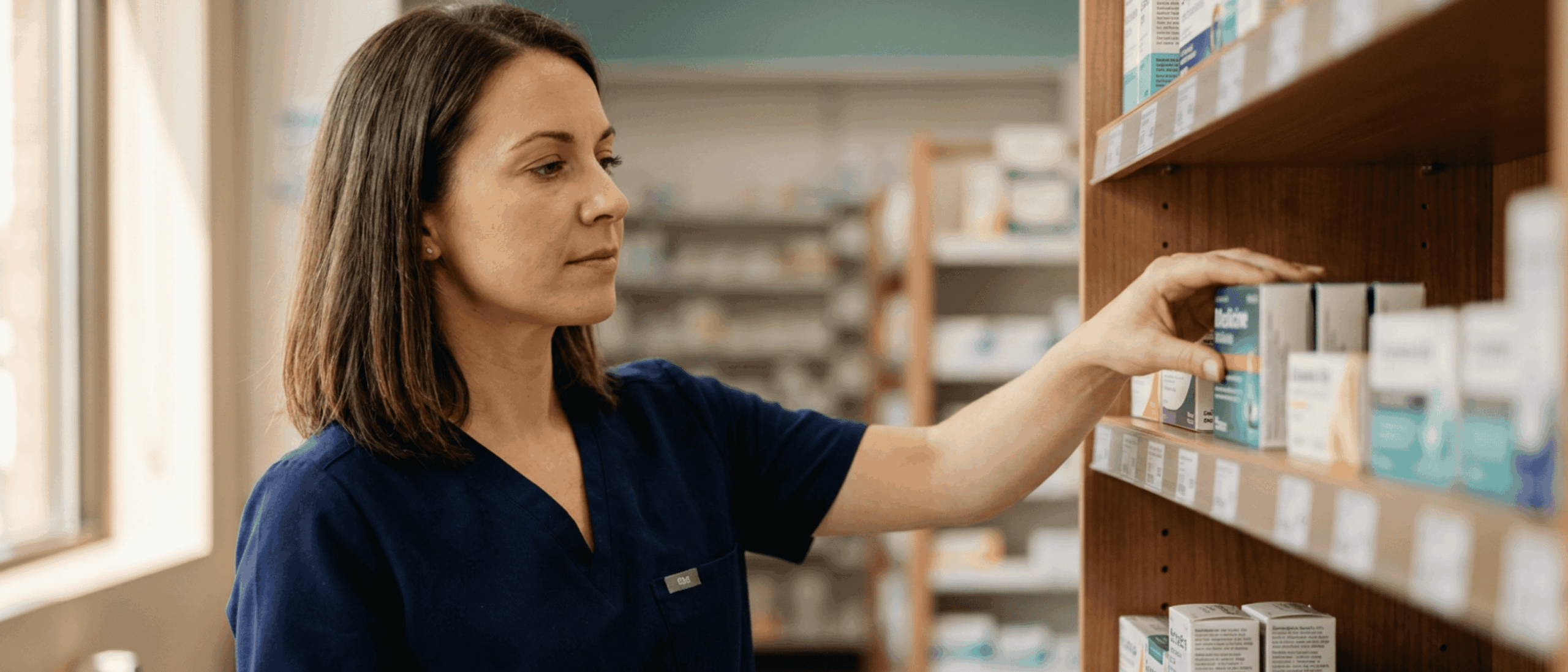A pharmacy technician reaching for medication on a shelf